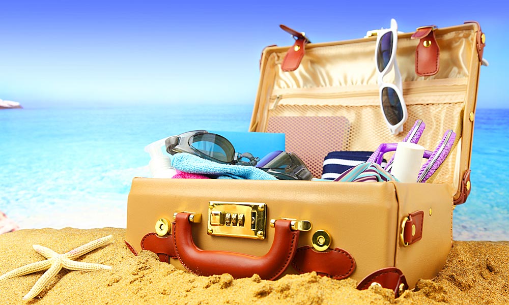 Urlaubskoffer am Strand mit Reise-Essentials